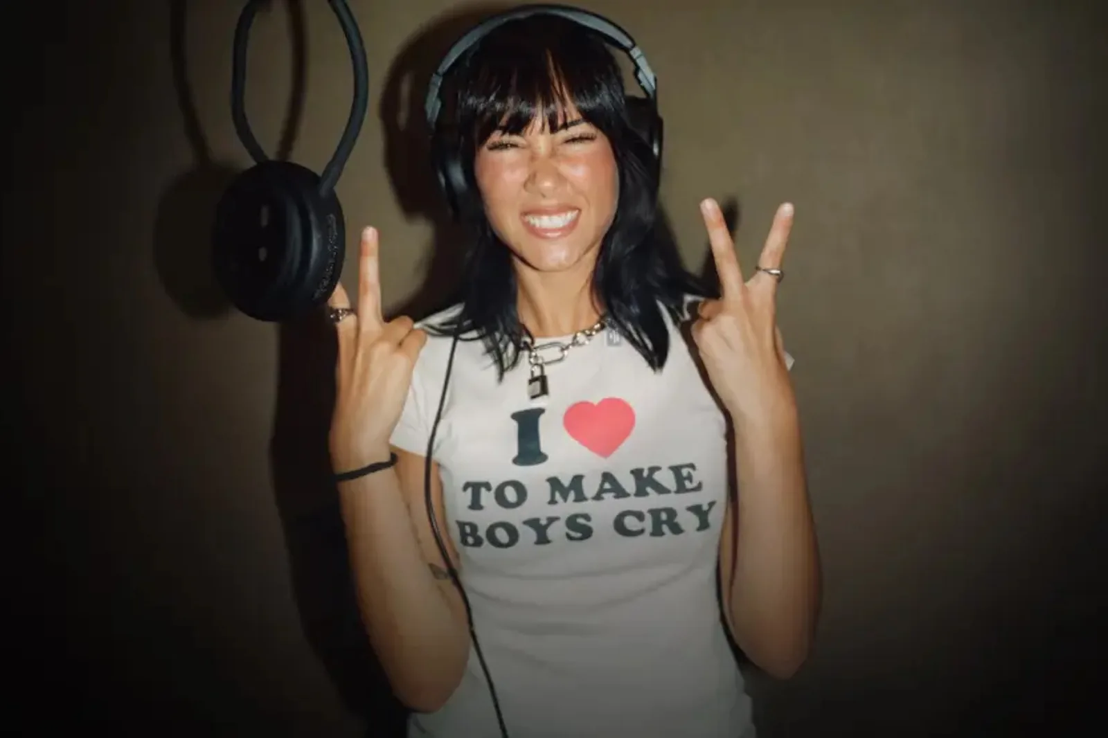 Aitana sonriendo junto a un micrófono y levantando dos dedos